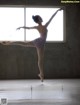 A young ballerina in a pink leotard and pointe shoes in front of a window.