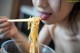 A woman eating noodles with chopsticks in her mouth.