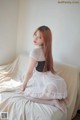 A woman sitting on top of a bed in a white dress.