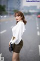 A woman in a white shirt and brown skirt standing on the street.