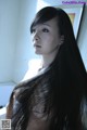 A woman with long black hair standing in front of a window.