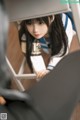 A woman in a school uniform leaning against a chair.