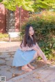 A woman in a blue skirt crouching down on a sidewalk.