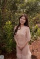 A woman in a pink dress standing in front of a bush.