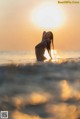 A woman standing in the ocean at sunset.