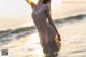 A woman in a white dress standing in the ocean at sunset.