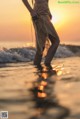 A woman standing in the ocean at sunset.