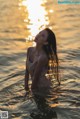 A woman standing in the water at sunset.