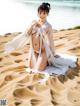 A woman in a white dress sitting on a sandy beach.