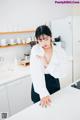 A woman in a white shirt and black skirt standing in a kitchen.