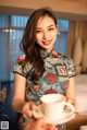 A woman in a cheongsam holding a cup of coffee.