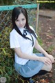 A woman in a school uniform sitting on the ground.