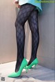 A woman wearing black tights and green high heels.