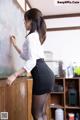 A woman in a skirt and glasses writing on a blackboard.