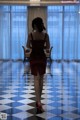 A woman in a red dress walking down a checkered floor.