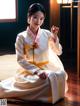 A woman in a white and yellow hanbok sitting on the floor.