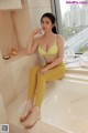 A woman sitting in a bathtub wearing a yellow bra and leggings.