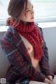 a woman sitting on a window sill wearing a red scarf