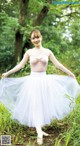 A woman in a pink top and white tutu standing in the woods.