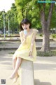 A woman in a yellow dress sitting on a concrete pillar.