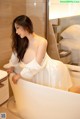 A woman in a white dress sitting in a bathtub.