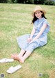 A woman in a blue dress and straw hat sitting on the grass.