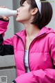 A woman in a pink jacket drinking from a bottle.