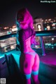 A woman with pink hair standing on a balcony at night.