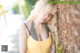 A woman in a yellow tank top leaning against a tree.