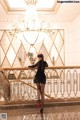 A woman in a black dress standing in front of a chandelier.