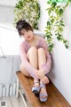 A woman sitting on a wooden bench next to a plant.