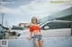 A woman leaning against a fence in a parking lot.