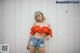 A woman in a red top and denim shorts posing for a picture.