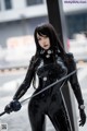 A woman in a black latex outfit holding a sword.