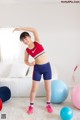 A young woman in a red sports bra top and blue shorts posing for a picture.