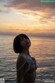 A woman in a bikini standing on the beach at sunset.