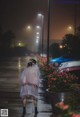 A woman walking down a sidewalk in the rain at night.