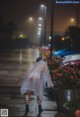 A woman walking down a sidewalk in the rain at night.