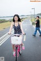 A woman riding a pink bike down a street.