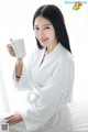 A woman in a white robe holding a cup of coffee.