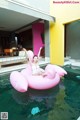 A woman sitting on an inflatable pink flamingo floating in a pool.